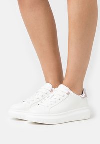 Weiße Leder-Sneaker mit abgerundeter Spitze, Schnürdesign und glänzenden roségoldenen Akzenten an der Ferse. Flache Sohle mit strukturiertem Grip.