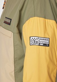 Giacca a blocchi di colore con pannelli verde oliva, beige e giallo. Tessuto texturizzato con un logo sulla manica e cuciture a contrasto.