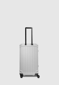 Hard-shell suitcase in matte white, featuring vertical ribbed texture, black retractable handle, and four wheels for mobility.