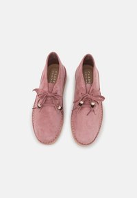 Zapatos de ante rosa con punta redondeada, cordones en la parte delantera y doble costura en la suela. El interior cuenta con un forro beige.