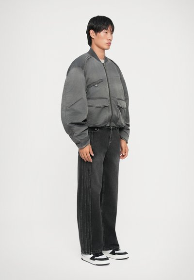 Gray bomber jacket with large pockets, paired with black wide-leg jeans featuring side seams. Worn with black and white sneakers.