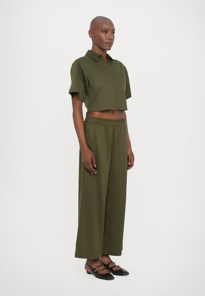 Chemise verte olive courte à manches courtes avec col, assortie à un pantalon ample et des chaussures plates noires avec des accents de sangle.
