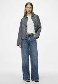 Giubbotto di jeans con righe bianche verticali, bottoni argentati, abbinato a jeans blu a vita alta e gamba larga e una maglietta bianca aderente.