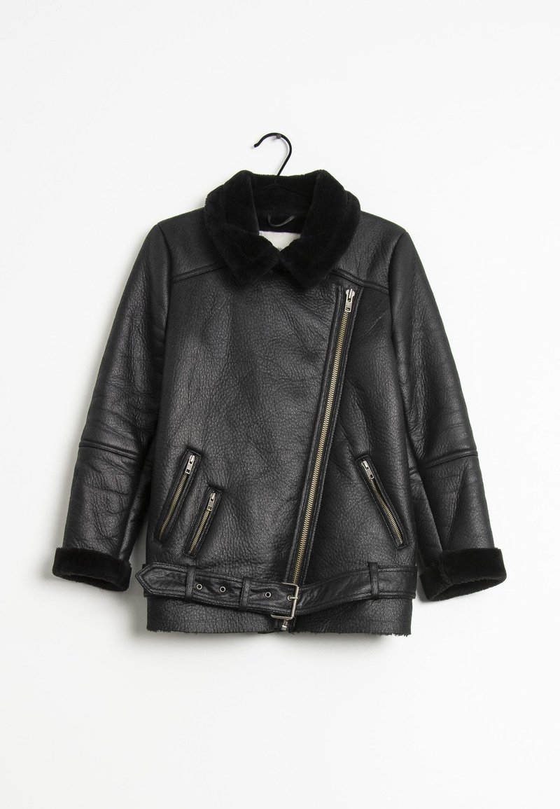 Veste en cuir noire avec col et poignets en fourrure, fermeture éclair asymétrique à l’avant, trois poches zippées et une ceinture à la taille, suspendue à un crochet.