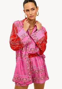 Vestido de camisa con patrón de bandana en rosa y rojo, de mangas largas, cintura elástica y un corte holgado. Presenta colores contrastantes y detalles intrincados.