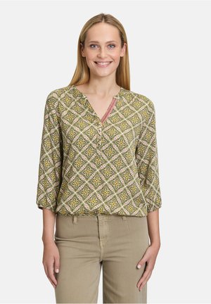 Blouse à motif floral en vert, jaune et rose. Présente un col en V, une patte de boutonnage et des manches trois-quarts. Texture de tissu lisse.