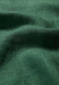 Tamsiai žalia lininė medžiaga su tekstūruota paviršiumi, rodanti švelnias klostes ir natūralų, švelnų jausmą.