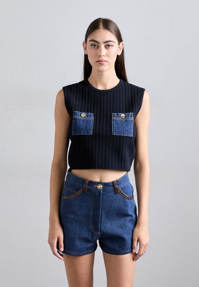 Černý žebrovaný crop top s dvěma kapsami z denimu. Vytvořený v kombinaci s džínovými šortkami s vysokým pasem, které mají hnědé akcenty a zlatý knoflík.