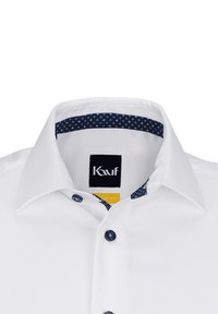 Weißes Hemd mit strukturierter Oberfläche, blauen Knopfakzenten und einem gemusterten marineblauen Kragenfutter. Verfügt über einen klassischen Kragen und eine Knopfleiste auf der Vorderseite.