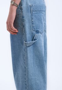 Light blue denim pants with a relaxed fit, featuring a single rear pocket and a side loop detail for additional storage.