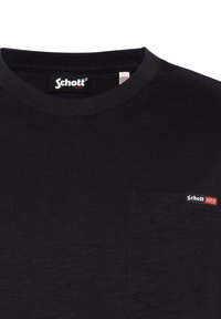T-shirt nera a girocollo realizzata in cotone, con una piccola tasca sul petto sinistro con etichetta rossa e bianca "Schott NYC". Texture liscia.