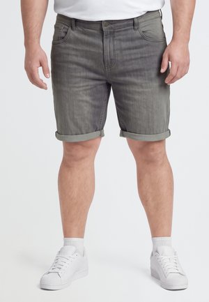Un mannequin porte un short en jean gris à revers, un tee-shirt blanc, des chaussettes et des baskets sur un fond uni.