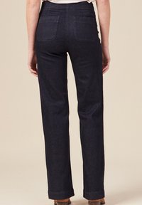 Pantalons en denim foncé avec une coupe droite, taille moyenne, deux poches arrière et ourlets retroussés. Texture lisse, détails de couture minimaux.