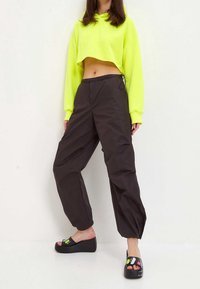 Neonowo-żółta krótka bluza z kapturem, czarne luźne spodnie oraz czarne koturny z kolorowymi akcentami. Gładka faktura i swobodny krój.