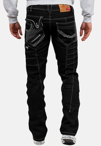 Jeans neri con cuciture bianche, molte tasche e design unici per le tasche posteriori. Realizzati in denim con una vestibilità regolare.