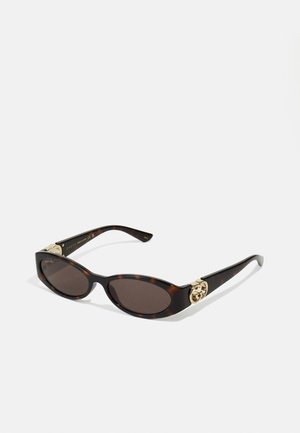 Óculos de sol de tartaruga com lentes ovais alongadas, tom castanho, acentos de logotipo dourado nas hastes e hastes pretas elegantes.
