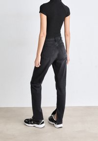 Black ribbed bodysuit paired with high-waisted black jeans featuring split hems and back pockets, worn with black and white athletic shoes.