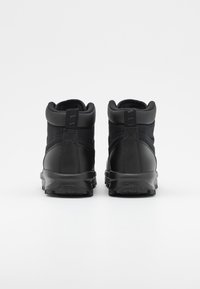Svarte høye sneakers med et teksturert stoffoverdel, glatte lærdetaljer og gummisåle. Designet har en polstret krage og en stropp bak.