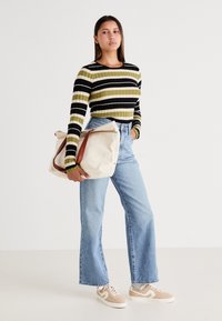 Stripet ribbet langermet topp i svart, oliven og gull; lyseblå høy midje vide jeans; beige joggesko og en overdimensjonert kremfarget veske med brun stropp.