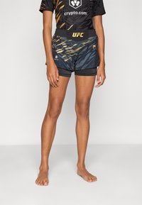 Fekete és arany UFC sort, geometrikus mintázattal, könnyű anyagból készült, rugalmas derékpánttal és hímezett logókkal.