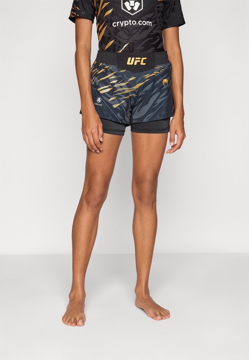 Fekete és arany UFC sort, geometrikus mintázattal, könnyű anyagból készült, rugalmas derékpánttal és hímezett logókkal.