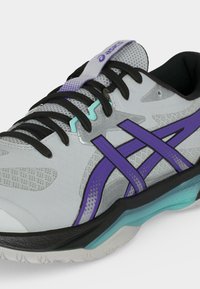 Αθλητικό παπούτσι Asics σε ανοιχτό γκρι και μοβ με μαύρα κορδόνια, δίχτυ στη γλώσσα και σόλα με τυρκουάζ λεπτομέρειες σε κοντινή προβολή.