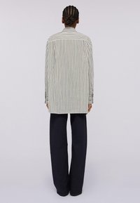 Camicia a righe con colletto, caratterizzata da righe verticali bianche e verdi. Abbinata a pantaloni ampi blu navy.