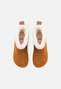 Bottines en daim marron avec doublure en fausse fourrure blanche et languette de traction. Bout rond et semelle plate, avec un label rouge sur la semelle intérieure.