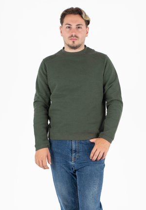 Donkergroen sweatshirt met lange mouwen en een ronde halslijn. Heeft een textuurdetail op de schouders en geribbelde manchetten. Draagt met een blauwe jeans.