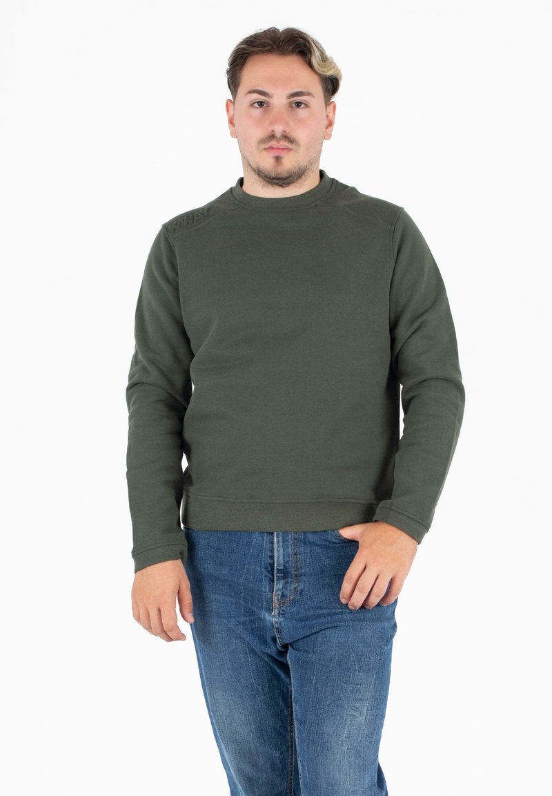 Donkergroen sweatshirt met lange mouwen en een ronde halslijn. Heeft een textuurdetail op de schouders en geribbelde manchetten. Draagt met een blauwe jeans.