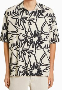 Košile s krátkým rukávem ve smetanové barvě s výrazným černým květinovým vzorem. Má rozšířený límec a volný střih; vyrobena z lehkého materiálu.