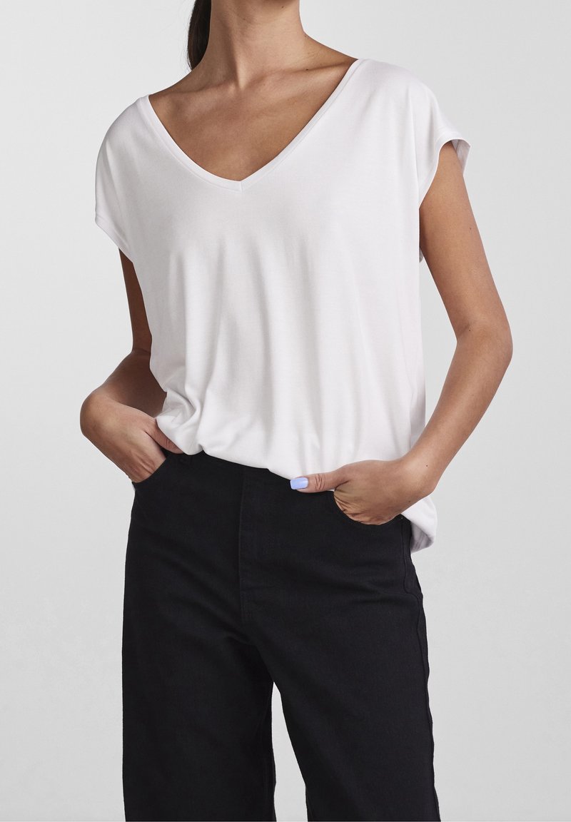 Vit kortärmad t-shirt med V-ringning och avslappnad passform, kombinerad med högmidjade svarta byxor. Slät textur, enkel design.