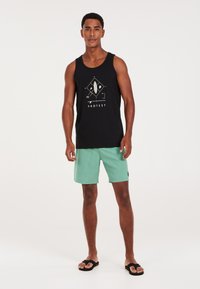 Canotta nera con design grafico e testo "PROTEST", abbinata a pantaloni corti verde menta. Infradito completano il look spiaggiato casual.