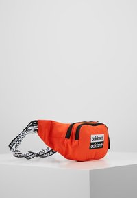 Orange canvas fanny pack with black zipper, featuring a logo patch and a striped adjustable strap. Compact, rectangular design.