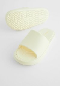 Sandales à enfiler ouvertes en mousse jaune douce avec une large lanière et une semelle extérieure texturée présentant un motif zigzag.
