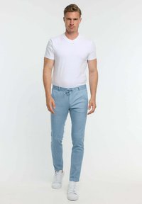 Weißes V-Ausschnitt-T-Shirt, hellblaue Hose mit Kordelzug, schlanker Schnitt, glatte Textur, getragen mit weißen Sneakers, vor einem schlichten Hintergrund stehend.