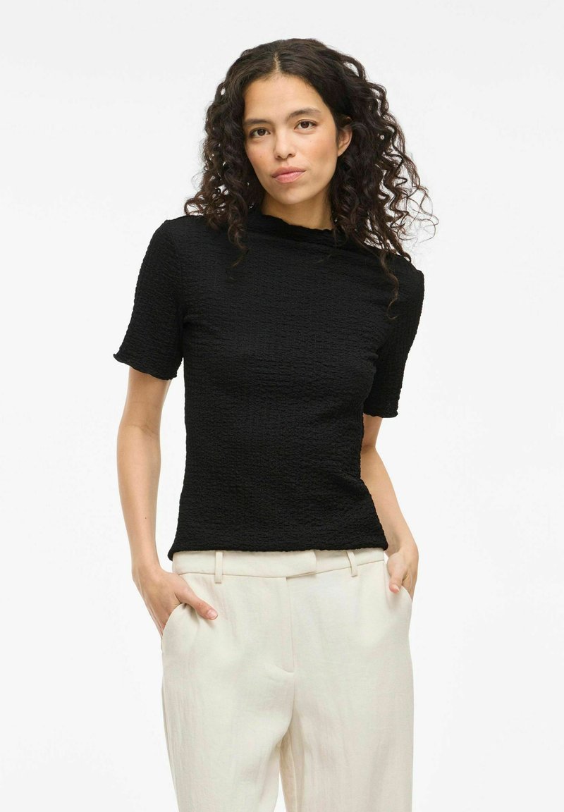 Top corto nera, con texture e collo alto, abbinato a pantaloni larghi di colore chiaro.