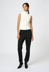 Prążkowany top bez rękawów z wysokim kołnierzem w kolorze kremowym, zestawiony z obcisłymi czarnymi spodniami i czarnymi, spiczastymi botkami za kostkę, tworzącymi opływową sylwetkę.