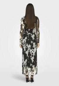 Langes, schwarz-weiß gepunktetes Kleid mit langen, durchsichtigen Ärmeln, tailliertem Schnitt und fließendem Saum. Getragen mit schwarzen hohen Schuhen.