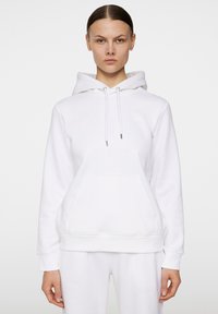 Vit hoodie med en framficka, dragsnöre vid huvan och ribbade ärmslut. Tillverkad av mjukt tyg med minimal branding. Slät textur, avslappnad design.