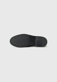 Suola di scarpa in pelle nera con texture liscia e un leggero tacco, cuciture visibili e un logo del marchio impresso nel materiale.
