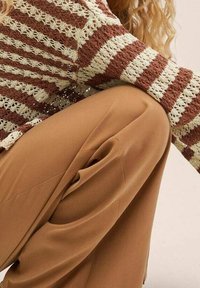 Strickpullover in Creme und braunen Streifen mit einem strukturierten Muster, kombiniert mit sandfarbenen, hochgeschnittenen Hosen im lockeren Schnitt.