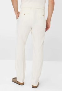 Pantaloni di lino bianchi a gamba dritta, con una tasca posteriore dotata di chiusura a bottone e una cintura comoda, abbinati a scarpe marroni slip-on.