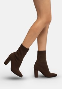 Braune gestrickte Stiefeletten mit spitz zulaufender Zehenpartie und klobigen Absätzen, ausgestattet mit einem gerippten Bündchen für eine bequeme Passform und einem strukturierten Stoffdesign.