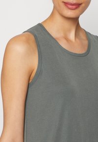 Grijze tanktop met een geribbelde textuur. Heeft een ronde halslijn en brede schouderbanden, en toont een zachte en ontspannen pasvorm.