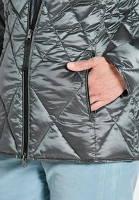 Gequilted grijze pufferjack met diagonale patroon, rits aan de voorkant en zijzak, gemaakt van glanzend, glad synthetisch materiaal.