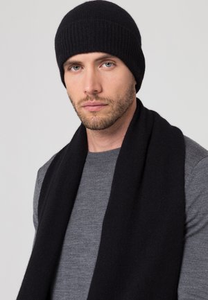 Berretto di maglia nera e sciarpa, texture morbida, indossato sopra una maglietta grigia a maniche lunghe, caratterizzato da un design aderente senza motivi.