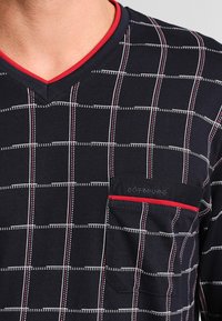 Marineblauw shirt met een wit en rood ruitpatroon, V-hals ontwerp, korte mouwen en een borstzak met logo en accentdetails.