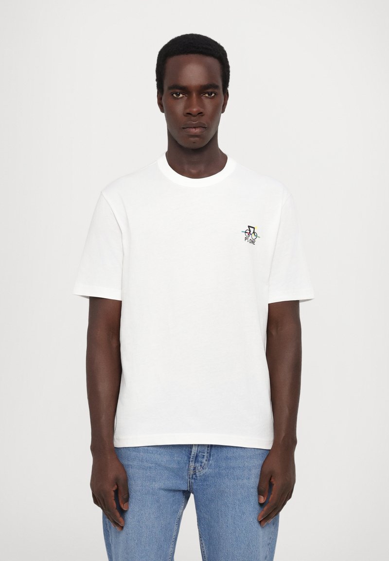 Camiseta blanca de algodón de manga corta con cuello redondo y pequeño logo colorido en el pecho, combinada con jeans azul claros.