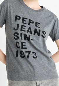 Camiseta de algodón gris con mangas cortas que presenta texto negro en relieve: "PEPE JEANS SINCE 1973", con un ajuste sencillo y clásico.